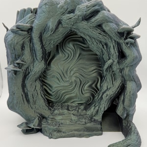 Op de afbeelding: Een gedetailleerde, donkergroene sculptuur van een portaal of deur, die lijkt op een knoestige boom met een wervelend, gestructureerd centrum. De sculptuur heeft een ruwe, organische textuur, met kleine paddenstoelachtige details. Het thema is fantasie of mystiek.