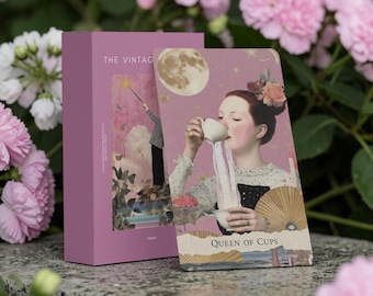 May include: A deck of tarot cards in a mauve box titled The Vintage, featuring a card titled Queen of Cups. The card displays a person pouring liquid from a teacup into another, with a full moon, flowers, and a parasol in the background.