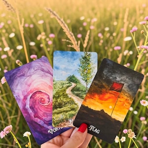 May include: Three rectangular tarot cards featuring artistic illustrations. The left card shows a purple and pink spiral vortex. The centre card depicts a green grassy hill with a path and tree. The right card shows a red flag at sunset with the text FLAG.