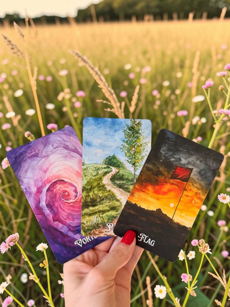 May include: Three rectangular tarot cards featuring artistic illustrations. The left card shows a purple and pink spiral vortex. The centre card depicts a green grassy hill with a path and tree. The right card shows a red flag at sunset with the text FLAG.