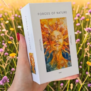 May include: A white rectangular tarot deck box titled Forces of Nature. The front features a vibrant watercolour illustration of a sun-faced figure with orange and yellow rays. Text includes Forces of Nature, Tools for Reflection, Healing and Connection, and Tarot.