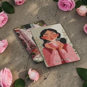 May include: Two decorative cards featuring illustrations. One depicts a woman holding a pink cup, with the text "Cup of Cozy." The other shows a European street scene. Pink roses and green leaves surround the cards.