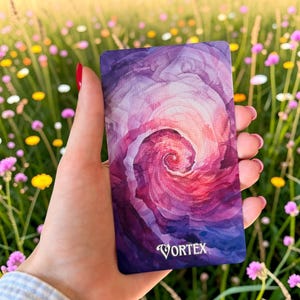May include: A rectangular card featuring a watercolour-style spiral design in shades of purple, magenta, and pink. The word VORTEX is printed in white capital letters at the bottom centre of the card, which has rounded corners and a smooth finish.