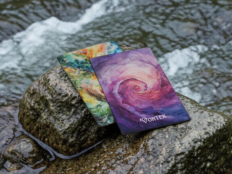 May include: Two rectangular cards with rounded corners. The front card features a purple and pink watercolour-style spiral design with the word VORTEX printed in white. The back card displays a multi-coloured abstract pattern of green, blue, and orange.