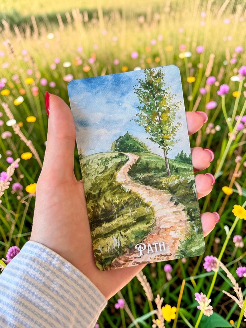 May include: A rectangular card featuring a watercolour illustration of a winding dirt path leading up a green grassy hill towards a blue sky with clouds. A single tall tree stands on the right side of the path. The word PATH is printed in white.