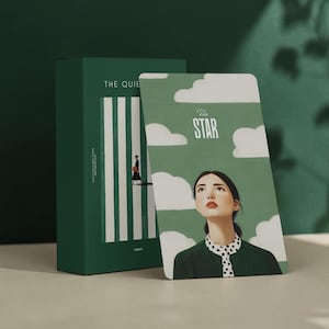 May include: A green tarot card deck and box set. The card features a woman looking up at the sky with clouds and the text "The Star." The box reads "The Quiet" with a minimalist illustration.