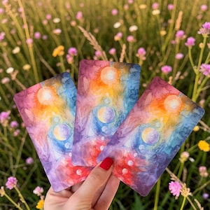 May include: Three rectangular cards featuring a vibrant watercolour design with swirling shades of purple, blue, orange, and yellow. Each card displays a central sun-like orb at the top, followed by a vertical sequence of smaller circular planetary shapes.