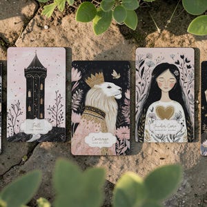 May include: A collection of tarot cards with various illustrations. The cards feature images of a tower, a lion with a crown, a woman with long hair, and a carousel. The color palette includes black, pink, and gold accents.