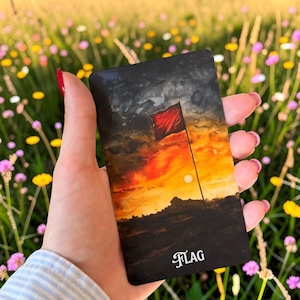 May include: A rectangular card featuring a painted illustration of a red flag standing on a dark horizon against a vibrant orange and yellow sunset sky. The word FLAG is printed in white, stylised serif lettering at the bottom of the card.