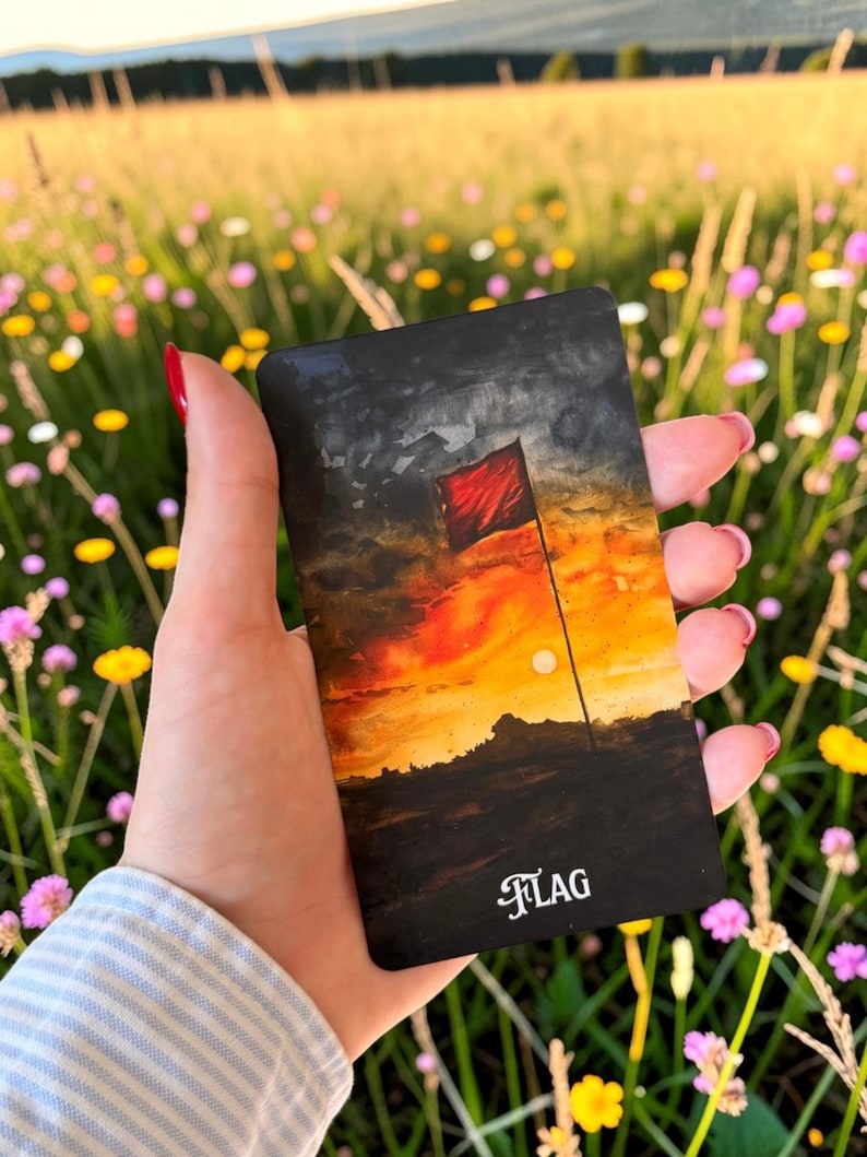 May include: A rectangular card featuring a painted illustration of a red flag standing on a dark horizon against a vibrant orange and yellow sunset sky. The word FLAG is printed in white, stylised serif lettering at the bottom of the card.