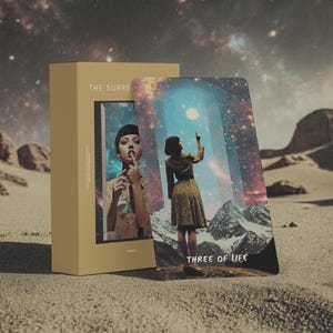 Pode incluir: Uma caixa retangular bege com o rótulo THE SURREAL e uma carta de tarô intitulada THREE OF LIFE. A carta mostra uma pessoa com um vestido estampado diante de um arco cósmico e montanhas, com uma segunda pessoa em uma imagem menor.