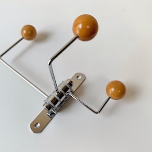 May include: A wall-mounted coat rack featuring a polished chrome metal base with three adjustable arms. Each arm extends outward and terminates in a smooth, round, mustard-yellow ball tip. The central mounting plate includes two screw holes.
