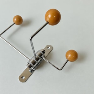 May include: A wall-mounted coat hook featuring a polished chrome metal base with three extending arms. Each arm is tipped with a smooth, round, honey-colored wooden ball. The central mounting plate includes two pre-drilled holes for installation.