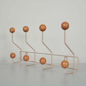 May include: A wall-mounted coat rack featuring a light beige metal frame with eight glossy, spherical wooden knobs in a warm tan colour. The structure consists of four vertical arms with alternating high and low hooks for hanging items.