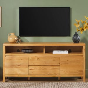 Può includere: Un mobile TV in legno di rovere chiaro con un grande televisore nero montato sopra. Il mobile ha due cassetti e ripiani aperti. Gli oggetti decorativi includono un vaso, una ciotola e un libro. Il mobile è largo 152 cm.