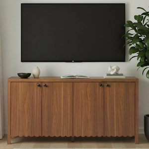 Op de afbeelding: Een houten tv-meubel met vier deuren en zwarte handgrepen. Het meubel heeft een geschulpte rand en is bekroond met decoratieve items, waaronder een zwarte kom, een witte vaas en een sculptuur. Een grote zwarte televisie is erboven gemonteerd.