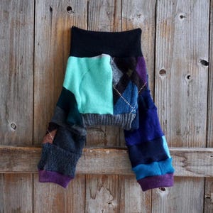 Può includere: Leggings per neonati patchwork realizzati con maglioni riciclati in tonalità turchese, blu, grigio e viola. I leggings hanno una cintura nera e polsini viola.