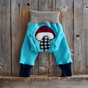 Puede incluir: Leggings de bebé de color azul turquesa con una aplicación de hongo en la parte posterior. El hongo es rojo, blanco y negro.