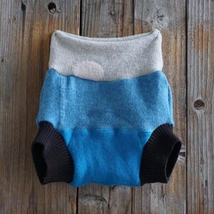 May include: A multi-colored baby diaper with a gray waistband, a blue midsection, and black leg cuffs. The diaper is made of soft fabric and is designed for comfort and absorbency. The diaper is displayed on a wooden surface.