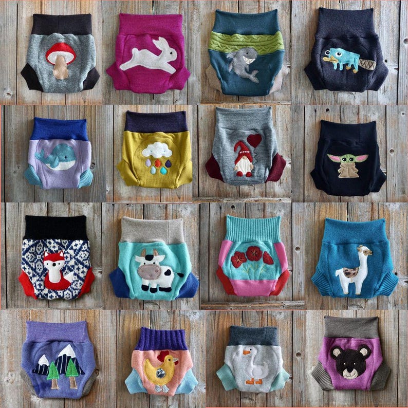 Może przedstawiać: Kolekcja 16 kolorowych, wielokrotnego użytku pieluch materiałowych z r&oacute;żnymi wzorami inspirowanymi zwierzętami i naturą. Każda pielucha ma inny haftowany wz&oacute;r, w tym kr&oacute;lika, rekina, gnoma, lamy, krowę, lisa, kurczaka, gęś, niedźwiedzia, wieloryba, grzyba, chmurę, g&oacute;rę, drzewo, kwiat i postać przypominającą Yodę.