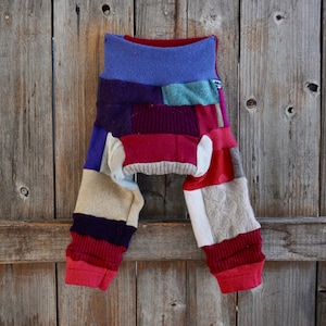 Puede incluir: Leggings de bebé patchwork hechos de suéteres reciclados en tonos de rojo, morado, azul, beige y blanco.