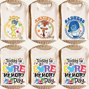 May include: Cream-colored t-shirts with various graphics. One shirt features "Joy" with a yellow dress and blue hair. Another displays "Anxiety" with a brown character. A third shows "Sadness". The bottom shirts read "Today is a Core Memory Day".