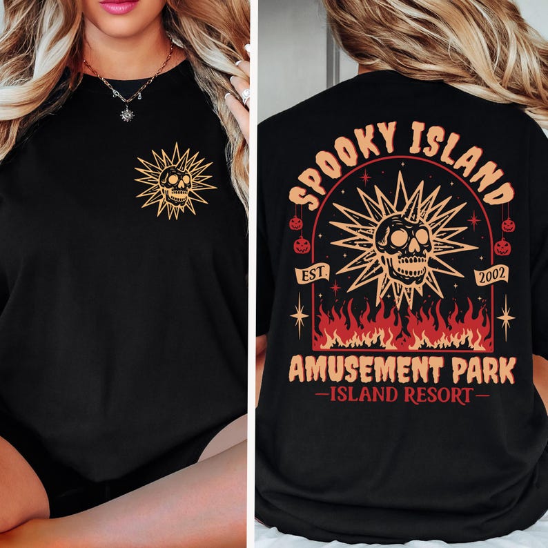 May include: Black t-shirt featuring a gold skull design within a sunburst on the front and back. The back of the shirt has the text "Spooky Island Amusement Park - Island Resort" with a skull and flames graphic. The shirt is a Halloween-themed item.