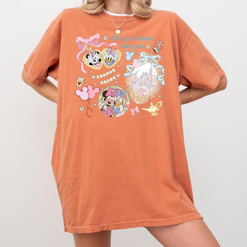 May include: Orange-colored t-shirt with a graphic design featuring Minnie Mouse, Daisy Duck, and a castle. The text "You only wanna have fun" is printed on the shirt. The design includes pink bows, a genie lamp, and a cupcake.