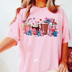 Puede incluir: Camiseta rosa claro con un dise&ntilde;o de personajes de dibujos animados y bebidas de caf&eacute;. El dise&ntilde;o incluye corazones, estrellas y personajes en azul, rosa y marr&oacute;n. La camiseta tiene cuello redondo y mangas cortas.