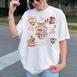 May include: White t-shirt with a colourful cartoon design. The graphic includes images of a cowboy, a space ranger, and other characters, along with the phrase "and beyond". The shirt has a relaxed fit.
