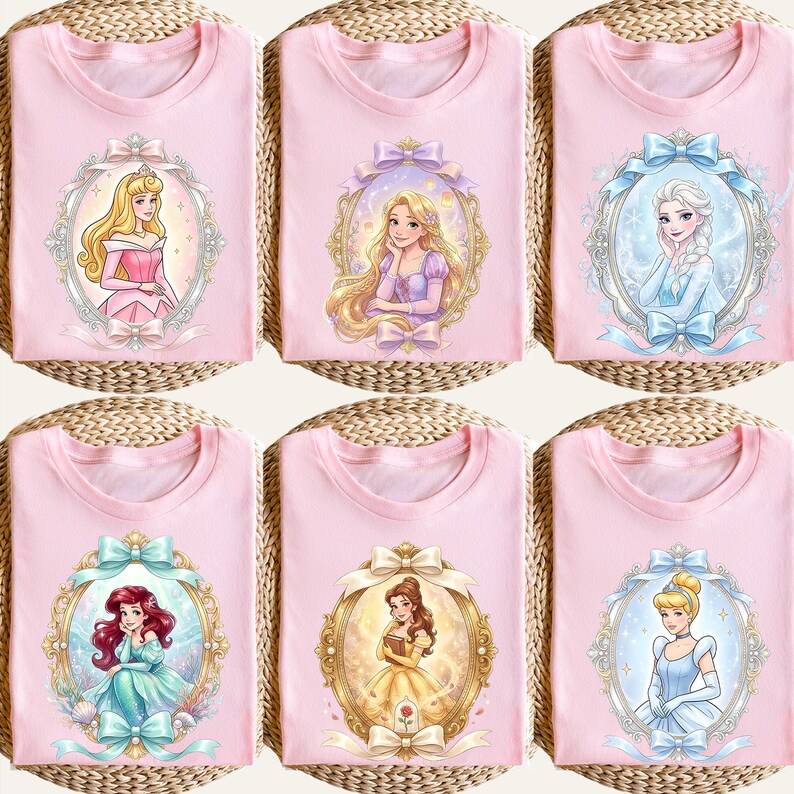 Op de afbeelding: Roze T-shirts met portretten van geanimeerde prinsessen in sierlijke frames. Elk shirt toont een andere prinses, waaronder Aurora, Rapunzel, Elsa, Ariel, Belle en Assepoester. De portretten zijn omgeven door decoratieve strikken.