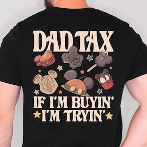 May include: Black t-shirt with the text "DAD TAX" and "IF I'M BUYIN' * I'M TRYIN'". The shirt features cartoon images of Mickey Mouse-themed treats and star shapes in various colors, including red, brown, and yellow.