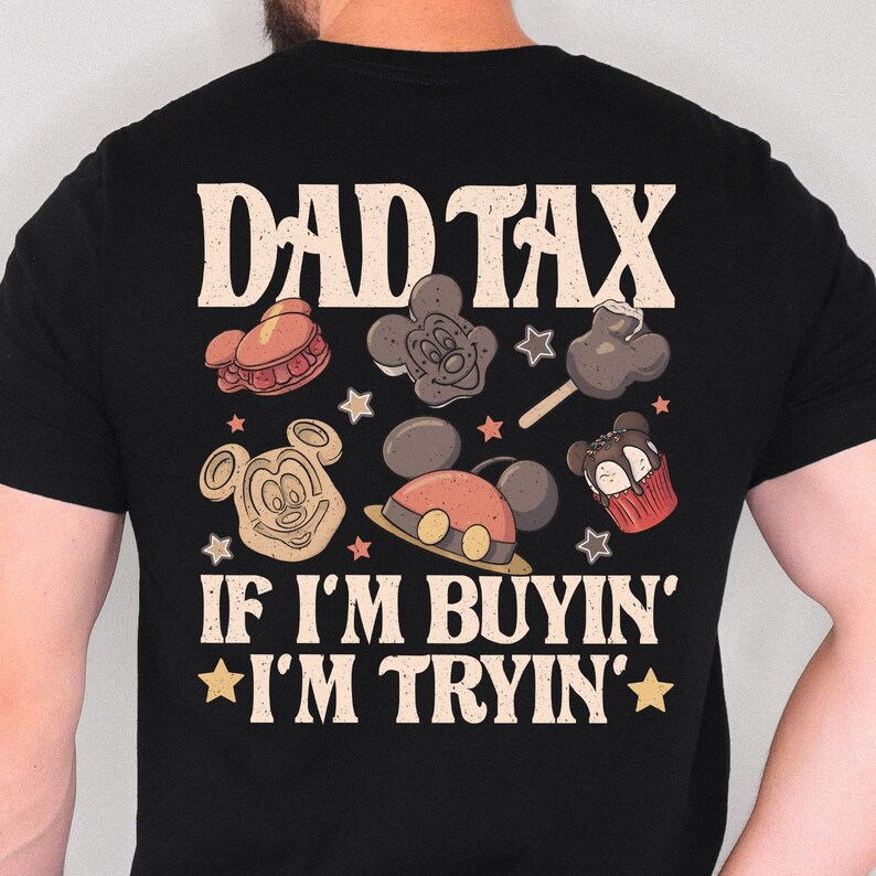 May include: Black t-shirt with the text "DAD TAX" and "IF I'M BUYIN' * I'M TRYIN'". The shirt features cartoon images of Mickey Mouse-themed treats and star shapes in various colors, including red, brown, and yellow.