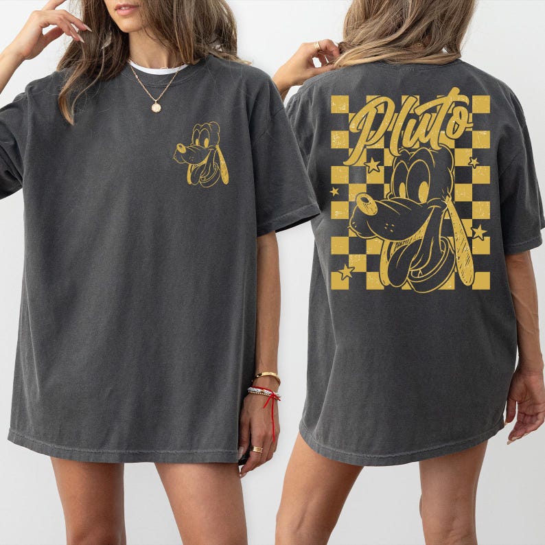 May include: Dark gray t-shirt featuring a gold cartoon Pluto graphic on the front and back. The back design includes the name "Pluto" in a script font, set against a gold and black checkered background with stars.
