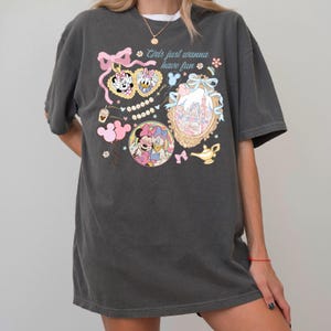 May include: Dark gray t-shirt featuring a colorful graphic with Minnie Mouse, Daisy Duck, and a castle illustration. The text "Girls just wanna have fun" is printed above the illustrations. The design includes pink bows, hearts, and other decorative elements.