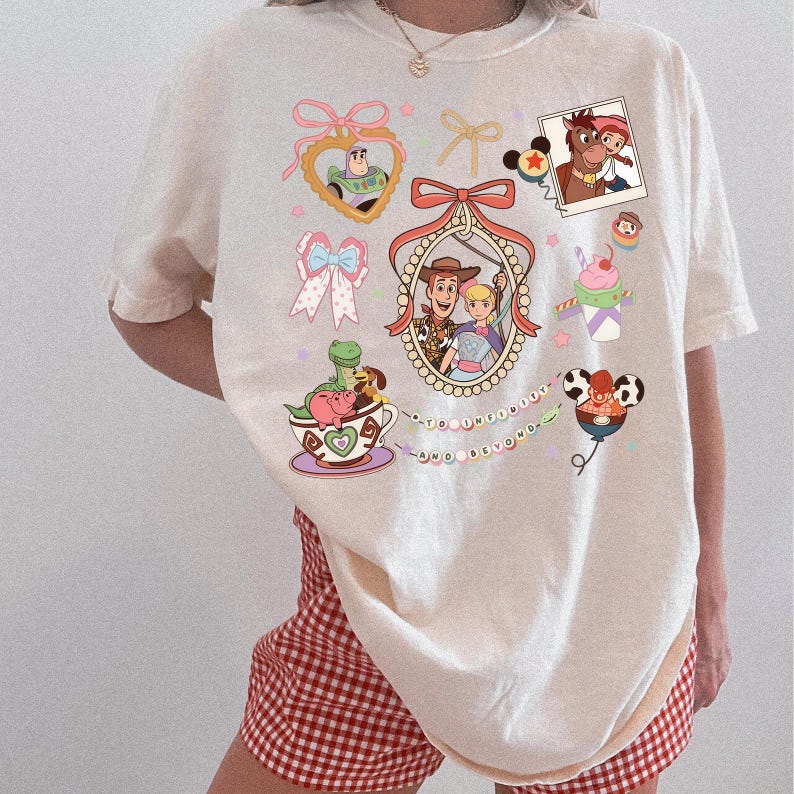 May include: Cream-coloured t-shirt with colourful cartoon graphics of Toy Story characters. The design includes Buzz Lightyear, Woody, Bo Peep, and other characters, along with the phrase "to infinity and beyond."