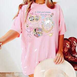 May include: Pink t-shirt with the text "Girls just wanna have fun" and various cartoon graphics. The graphics include Minnie Mouse, Daisy Duck, and a castle. The shirt is a loose fit.