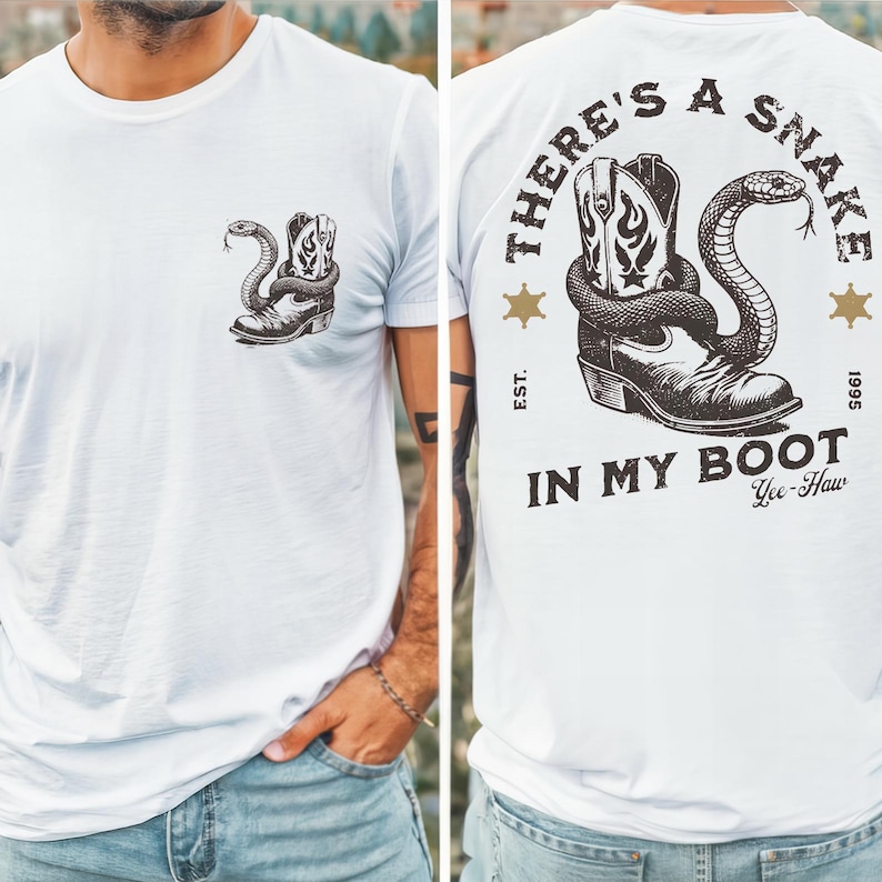 Pode incluir: Uma t-shirt branca com um pequeno gr&aacute;fico preto no peito esquerdo de uma cobra enrolada numa bota de cowboy. As costas exibem uma vers&atilde;o maior do mesmo gr&aacute;fico com o texto "THERE'S A SNAKE IN MY BOOT" e "EST. 1995".
