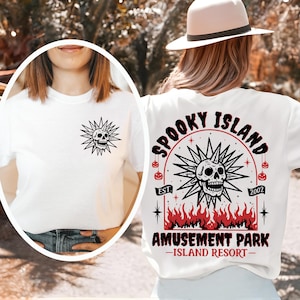 May include: White t-shirt featuring a black skull design with radiating lines on the front and back. The back design includes the text "Spooky Island Amusement Park - Island Resort" with a skull and flame graphic.