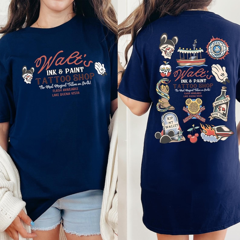 May include: Navy blue t-shirt featuring the text "Walt's Ink & Paint Tattoo Shop" with various tattoo-style graphics. The front of the shirt displays the shop's name and logo, while the back showcases multiple tattoo designs, including a skull, boat, and Mickey Mouse hand.