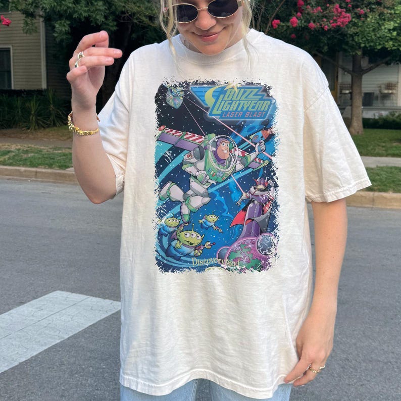 K&ouml;nnte beinhalten: Cremefarbenes T-Shirt mit einer farbenfrohen Grafik aus dem Film Toy Story. Die Grafik zeigt Buzz Lightyear, Aliens und den Text "Buzz Lightyear Laser Blast". Das Shirt hat eine lockere Passform.