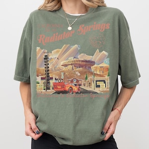 May include: A white ceramic mug with a black handle and the text "But First, Coffee" in a black, handwritten-style font. The mug is on a white surface.