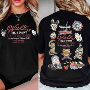 May include: Black t-shirt featuring the text "Walt's Ink & Paint Tattoo Shop" with various tattoo-style graphics. The design includes a skull, a boat, a snake, a tombstone, and a bottle with the text "Why's the rum gone?"