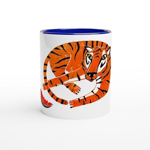 Può includere: Tazza in ceramica bianca con bordo interno blu con un'illustrazione di una tigre arancione con strisce nere. La tigre è arrotolata con una fetta di anguria. Un regalo divertente e unico per gli amanti degli animali.