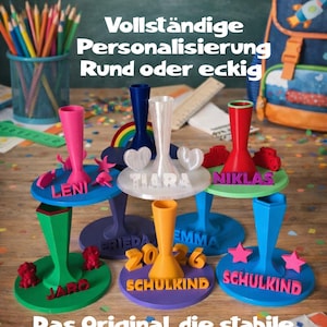 Könnte beinhalten: Eine Sammlung bunter, 3D-gedruckter Kunststoffständer für Schultüten in runder oder eckiger Form. Jeder Ständer ist mit Namen wie Leni, Tiara, Niklas, Jaro, Frieda und Emma sowie dem Text 2026 personalisiert und individuell gestaltet.