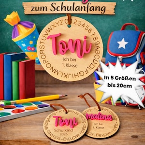 Op de afbeelding: Drie ronde houten hangers met bruine leren koorden. De grootste heeft de naam Toni in roze, het alfabet en de tekst Ich bin 1. Klasse. Twee kleinere hangers hebben de namen Toni en Malina met de tekst Schulkind 2026.