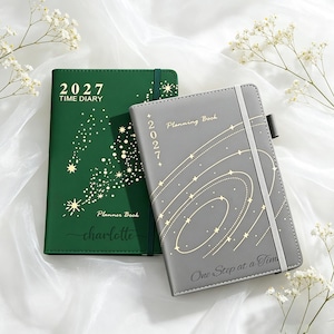 Peut inclure: Un agenda 2027 vert foncé avec des étoiles dorées et le nom Charlotte, accompagné d'un carnet de planification gris 2027 avec des motifs d'orbites étoilées dorées et le texte One Step at a Time, tous deux dotés d'élastiques de fermeture.