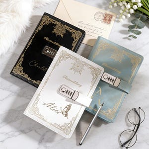 May include: An assortment of decorative journals with combination locks. The journals are black, white, and blue, with gold-colored ornate designs. One journal is labeled "Charlotte", another "Alice", and all have the word "Password diary".