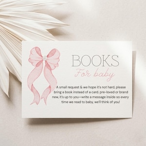 Op de afbeelding: Een rechthoekige witte kaart met een aquarelillustratie van een roze strik met een parel in het midden. De tekst luidt: BOOKS For baby. A small request & we hope it’s not hard, please bring a book instead of a card. Pre-loved or brand new.