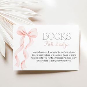 May include: A white card with the text "BOOKS For baby" and a watercolor illustration of a pink bow and ribbons. The card requests a book instead of a card, with a message inside. The background is a soft, neutral color.